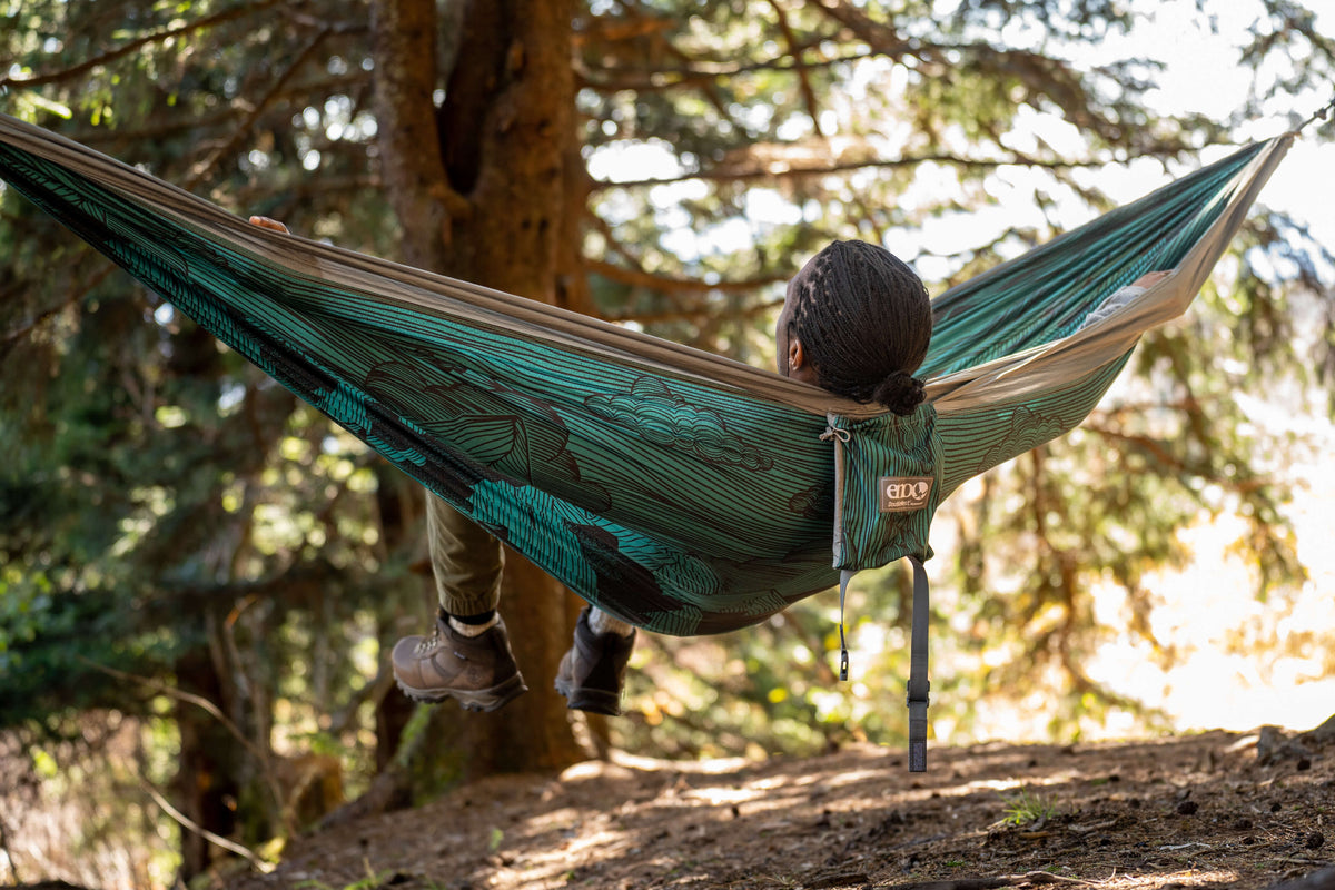 A man laying back in an ENO hammock looking at trees