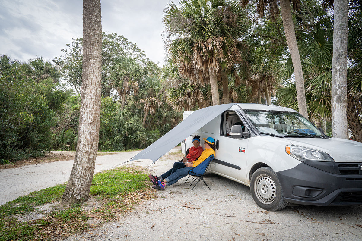 Two women sit under the ENO ProFly tarp connected to their van