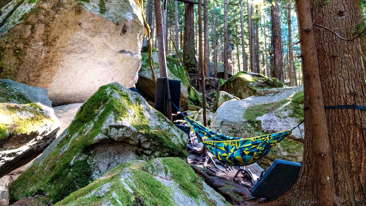 A person enjoys their DoubleNest Hammock Print near a big bouldering rock