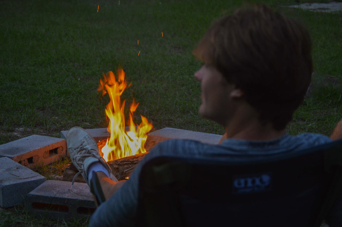 A person resting by a campfire in an ENO chair