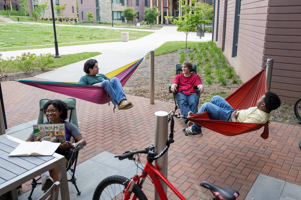 A group of 4 college students hammocking in an ENO Hammock and sitting in ENO Lounger Chairs in front of dorm