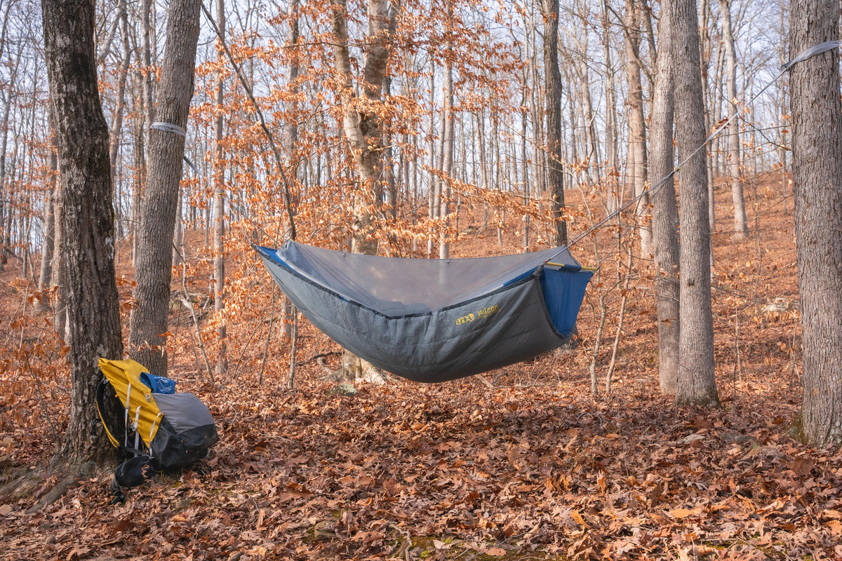An ENO SkyLite Hammock with an ENO Vulcan Vesta UnderQuilt. It is hung between two trees in the woods with orange fallen leaves under it