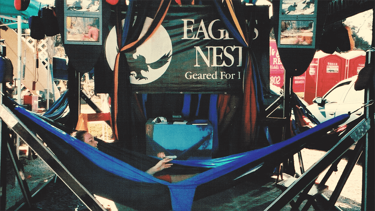 A person in an ENO hammock in an ENO hammock stand with an ENO banner behind them at a booth
