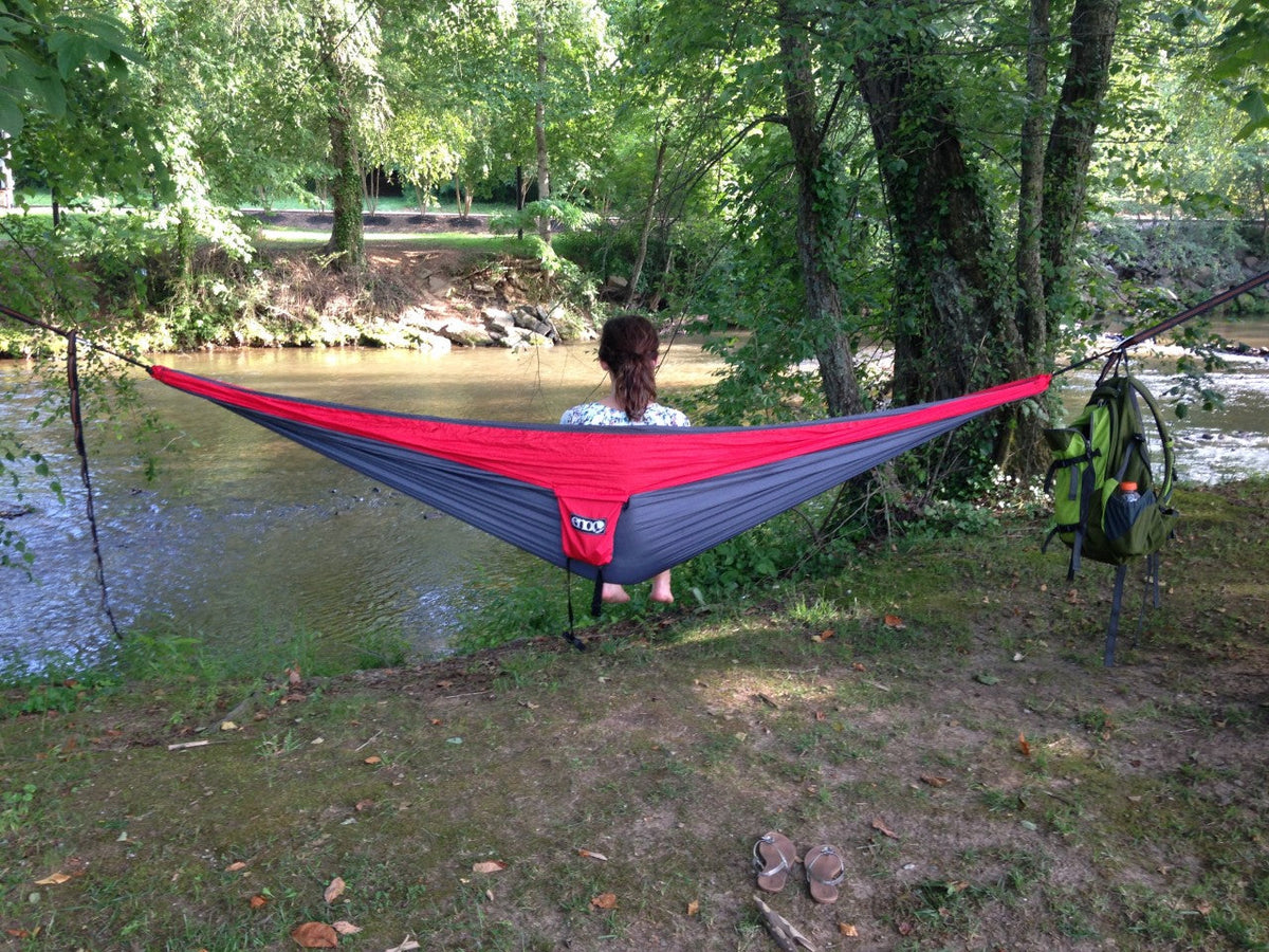A person hammocking in an ENO hammock by stream