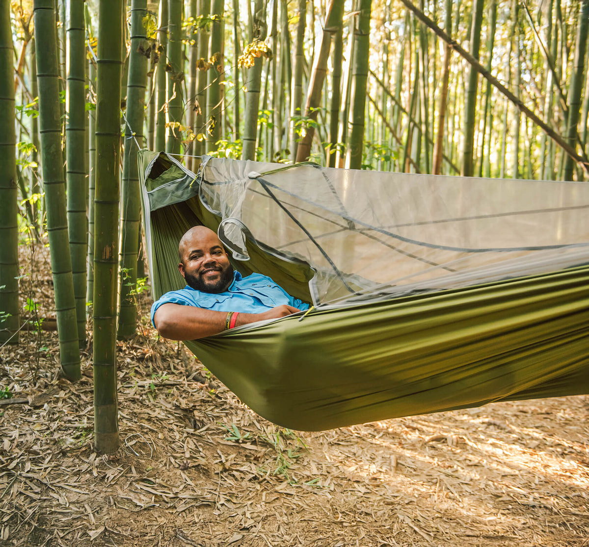 A man relaxing in the ENO JungleLink Hammock with integrated bug net surrounded by bamboo trees.