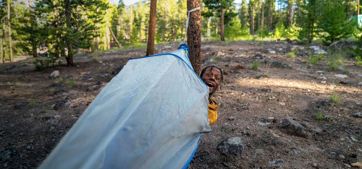 A young man pops his head out of the ENO JungleNest Hammock bug net hung with ENO Heilos Ultralight Hammock Straps while hammocking in the deep backcountry.