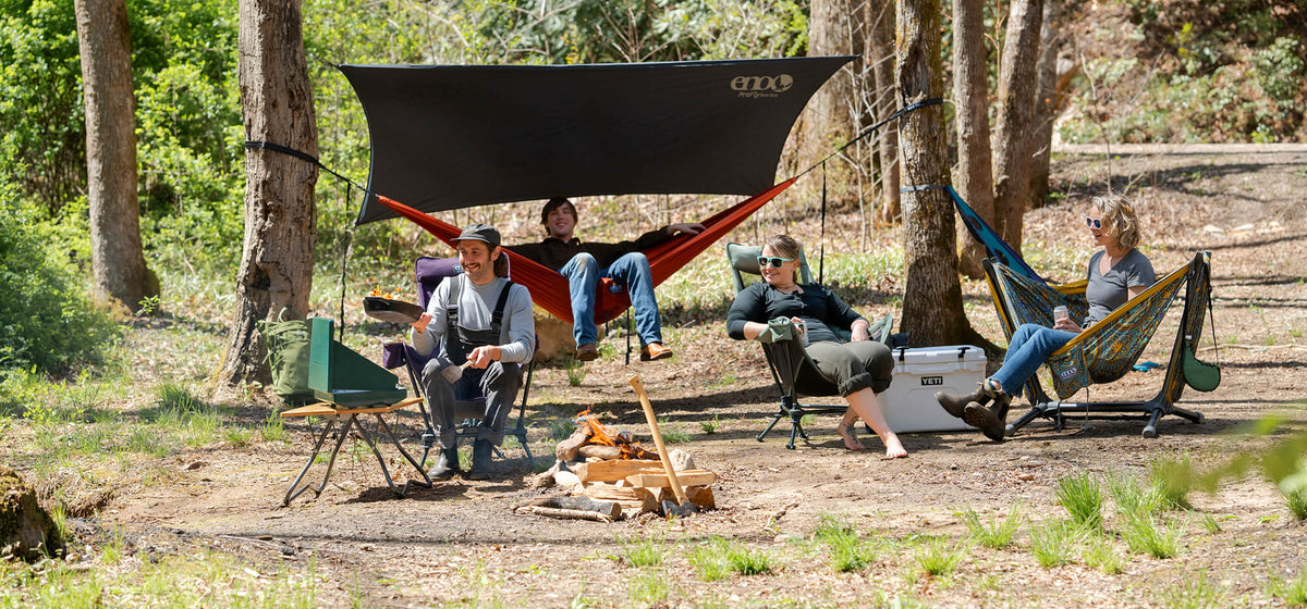 A group of people in a variety of ENO product within a camp basecamp watching a person cook.