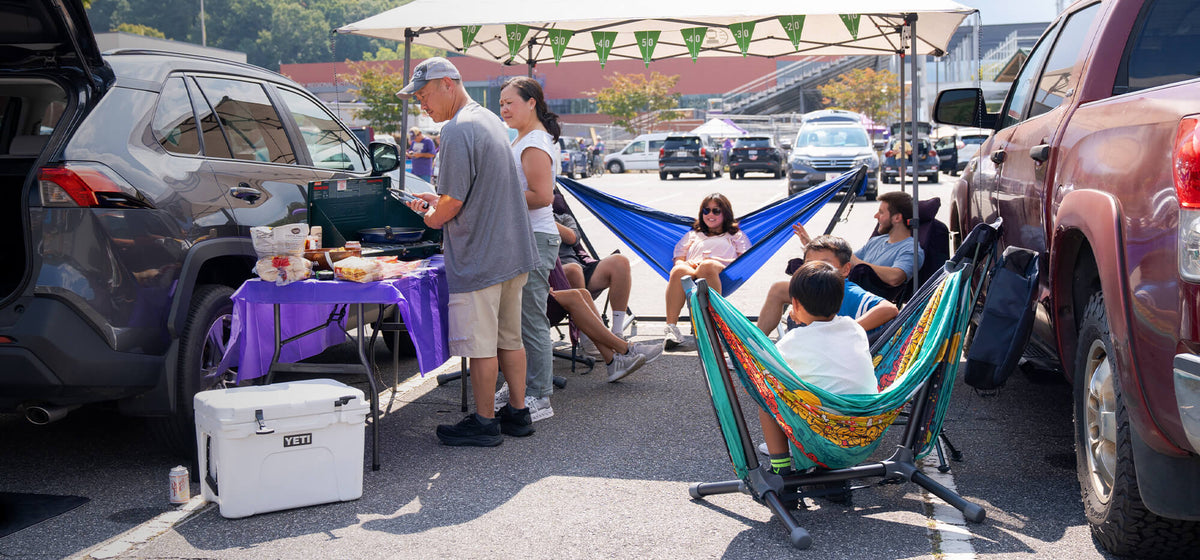 People using ENO hammocks, chairs, and stands in a parking lot tailgate setting.