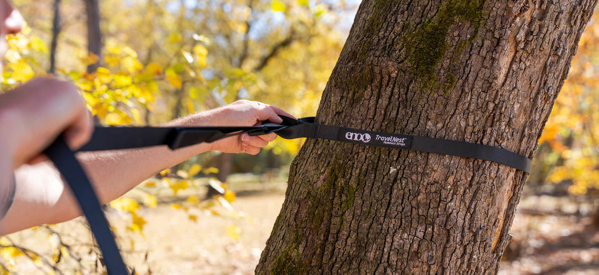 A close up image of a person setting up the hammock straps for the TravelNest Hammock + Straps Combo around a tree.
