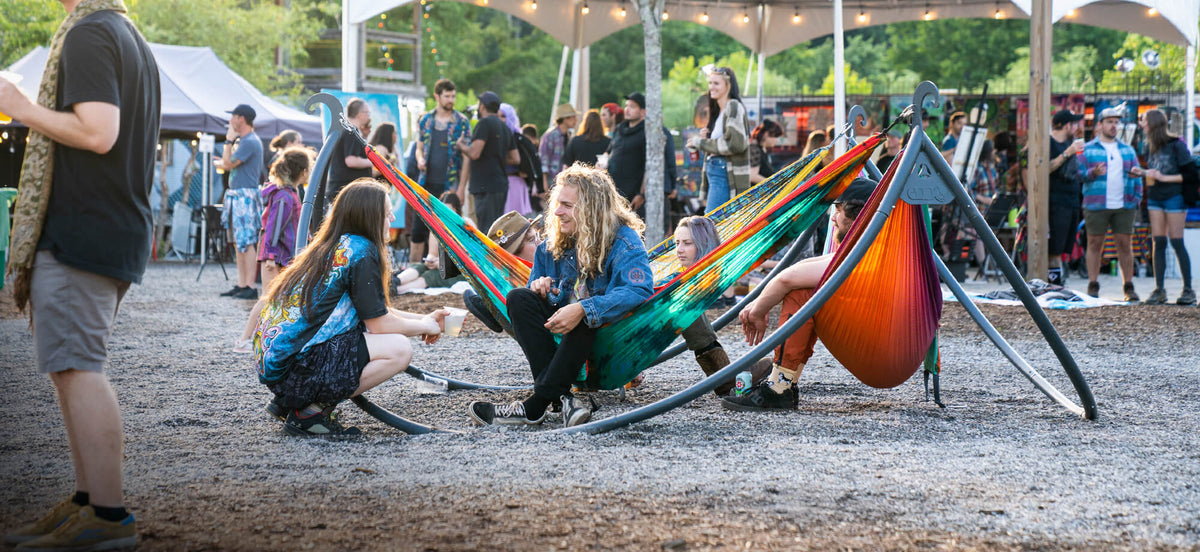 A group of people hand out in DoubleNest Hammock Prints set up on the ENOpod Triple Hammock Stand in a festival setting.