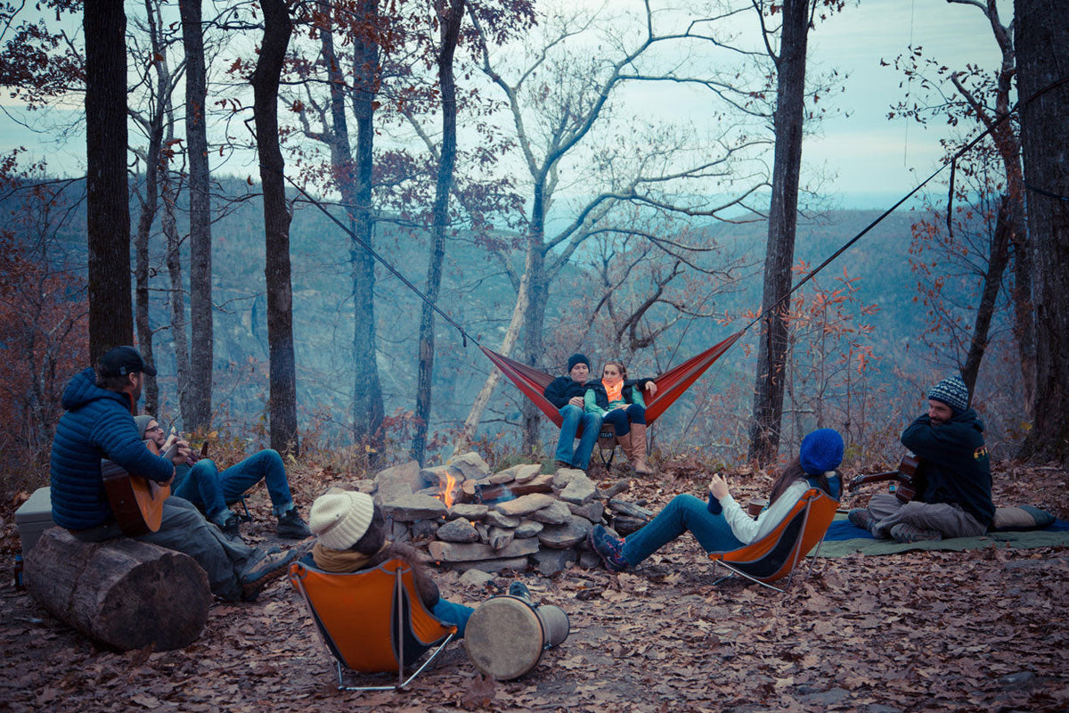 people sitting around a fire while camping in the woods with an ENO hammock