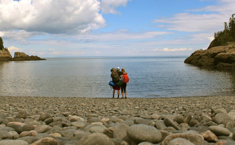 Chris and Laura on a rock shore looking at the ocean with backpacking gear on