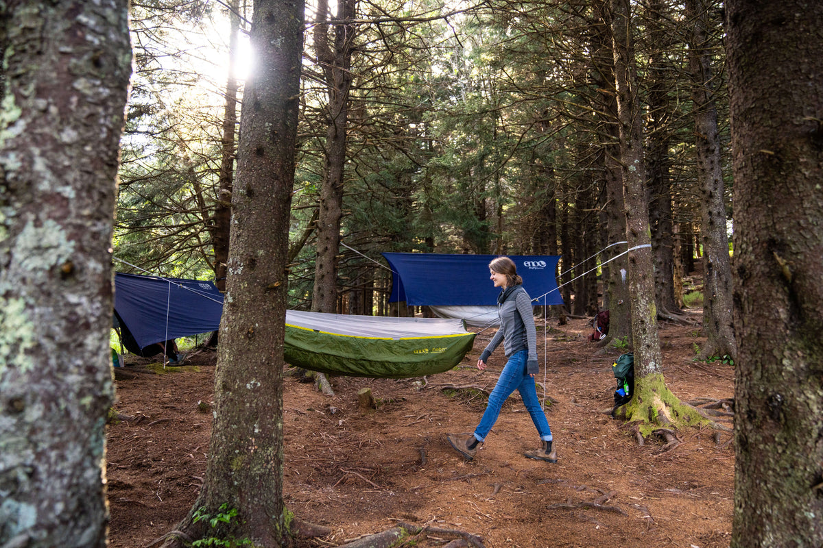 A woman walking through the woods with various ENO hammocks set up to camp