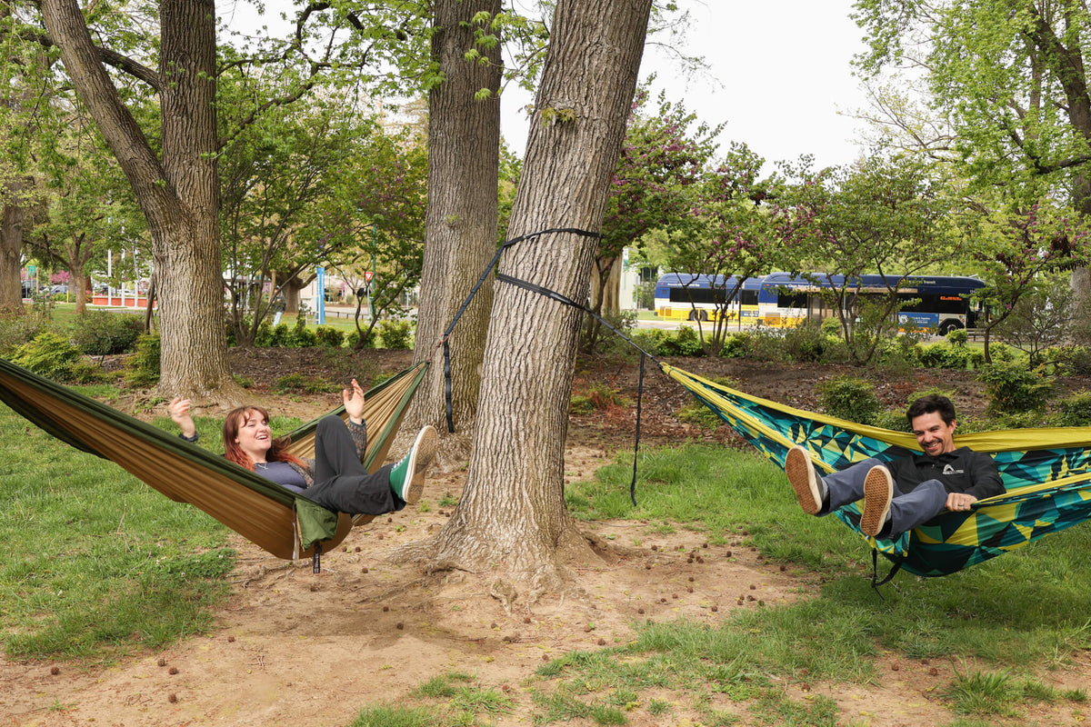 Two people hammocking in an ENO Hammocks separate hammocks with the city and busses in the background