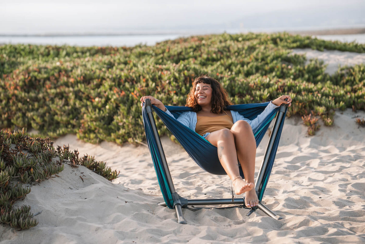A woman sits in her ENO Parklite Hammock Chair Stand  on the beach