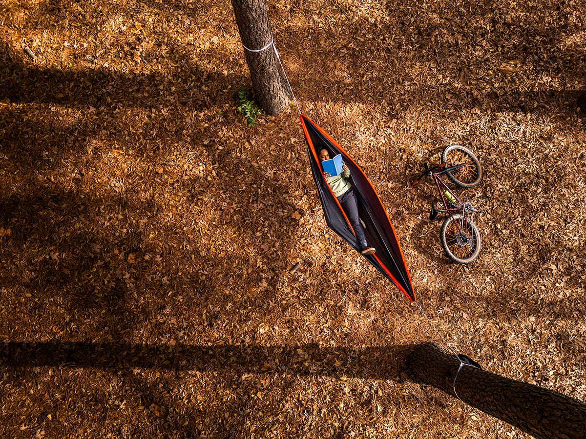 A person reading in an ENO Hammock with a bicycle next to it