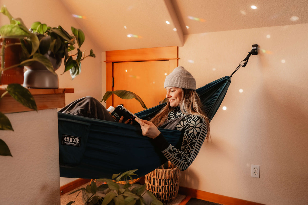 A woman is reading in an ENO TravleNest Hammock + Straps Combo inside. The hammock is hanging from the Hammock Hanging Kit.