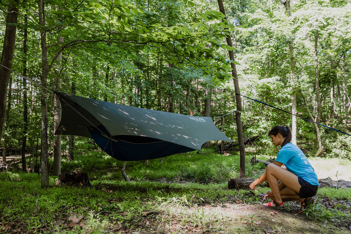 A woman setting up an ENO rain tarp over her ENO hammock in a forest
