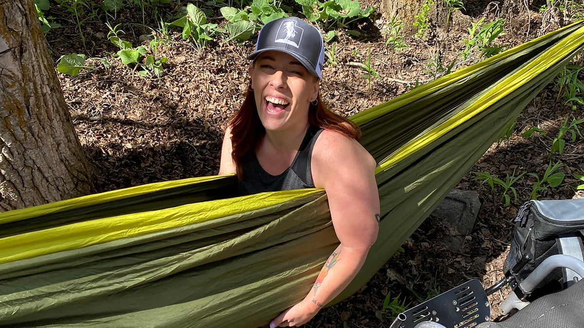 A woman smiles while sitting in an ENO hammock with her wheelchair nearby