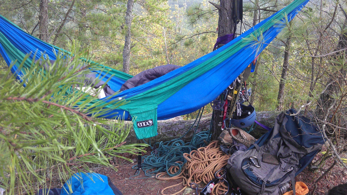 An ENO hammock strung between trees with various ropes and backpacks around it