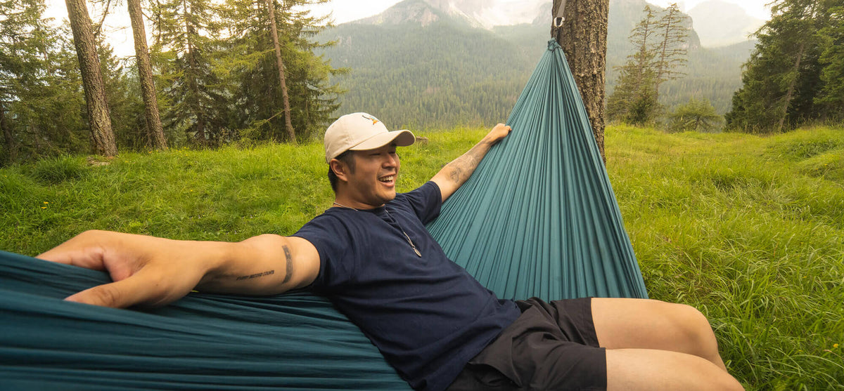 A woman sitting in a ENO portable hammock set up on a portable hammock stand in front of home. 