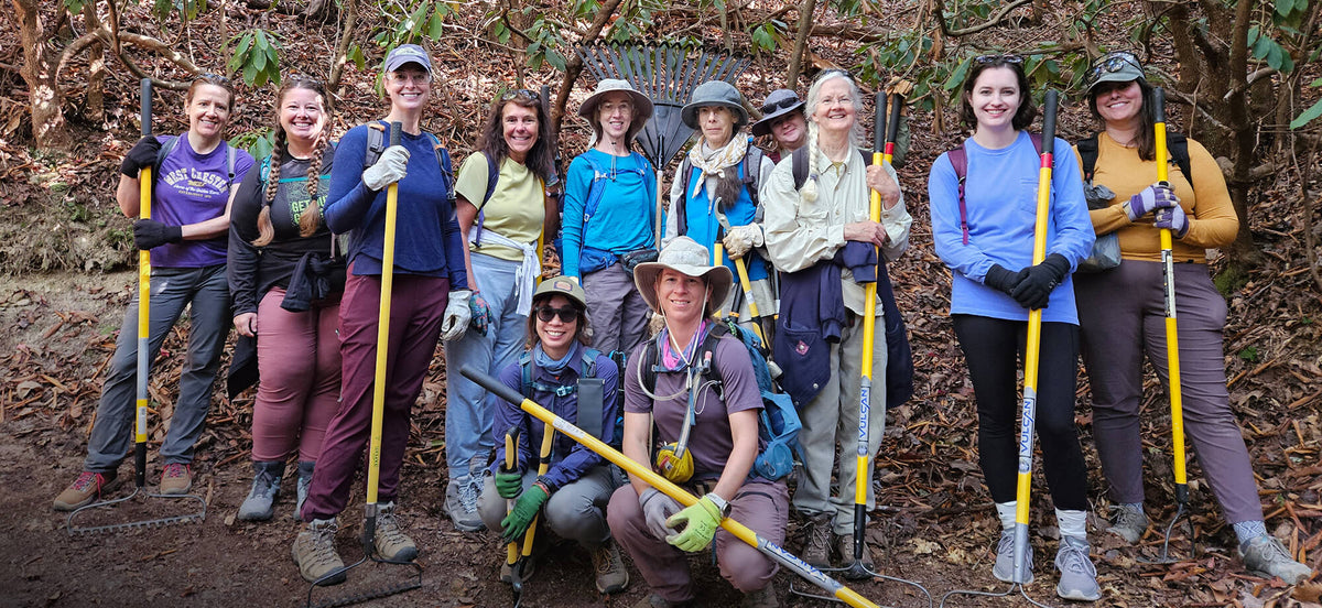 Group of people with tools posing for a photo in a forest setting