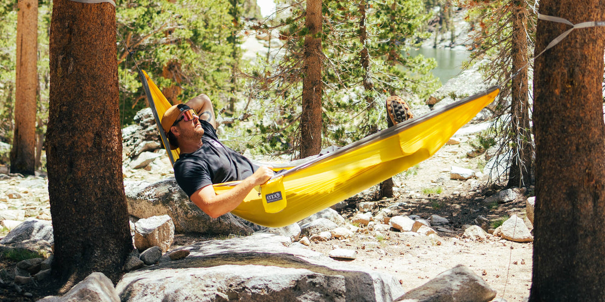 Person lying in a SuperSub Ultralight Hammock surrounded by trees and nature.