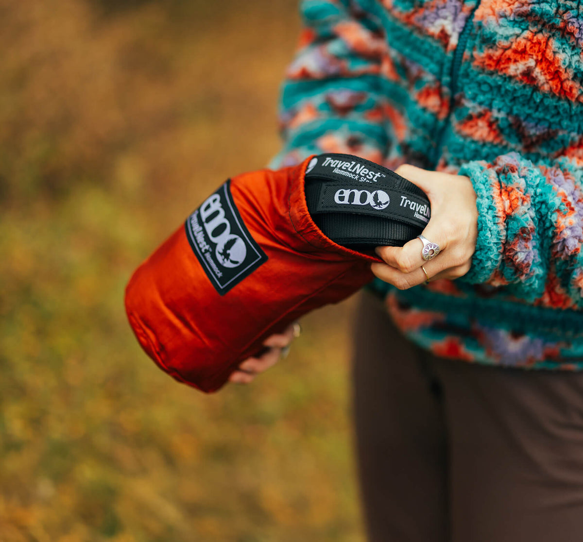 A close up image of a persons hand pulling the TravelNest Hammock + Strap Combo's straps out of the included stuff sack with a soft background.