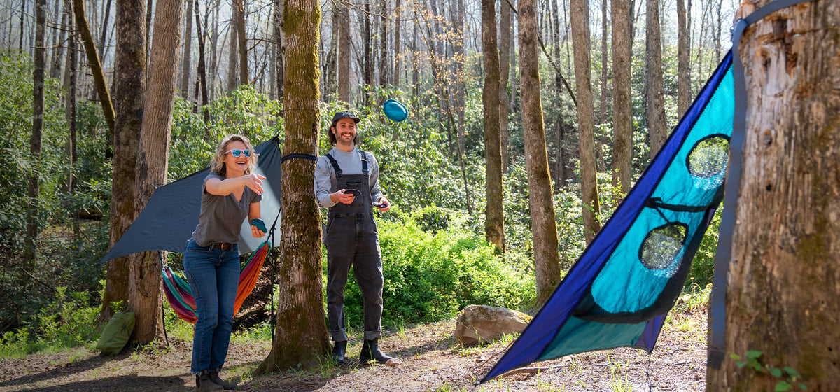 Two people laughing while playing ENO TrailFlyer Outdoor Game in a camp setting.