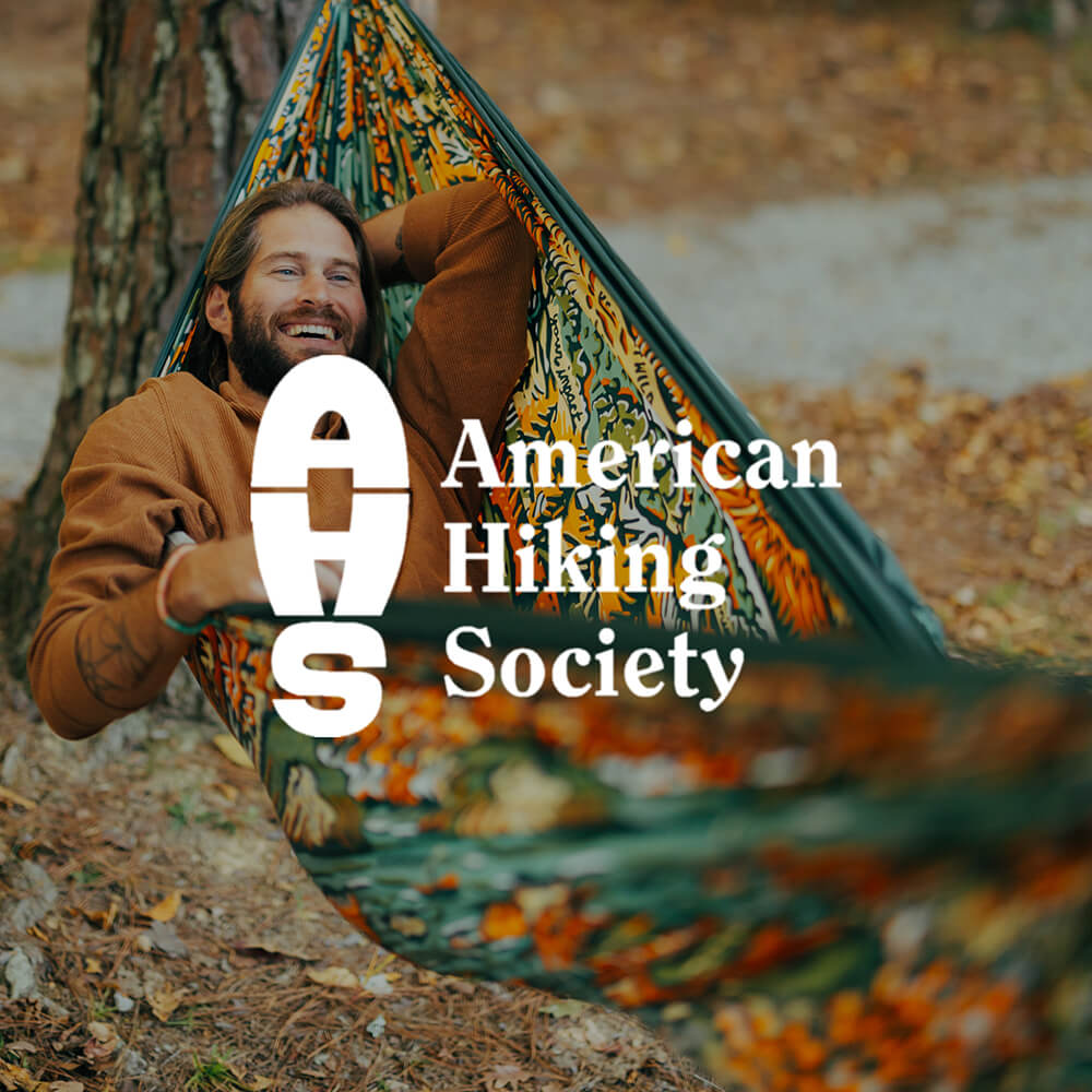 Person relaxing in the ENO Giving Back Hammock with the American Hiking Society logo overlay