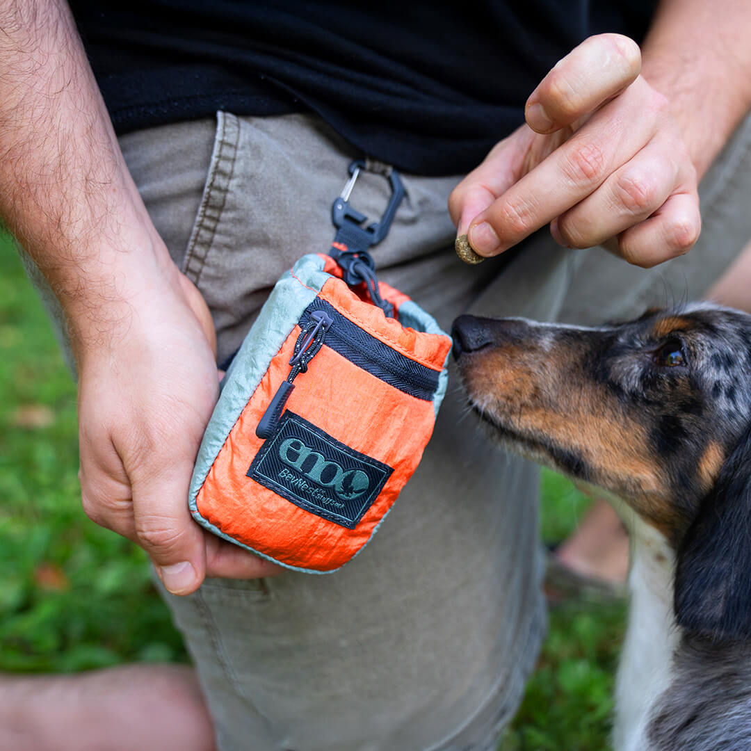ENO BevNest Stuff Sack worn around a person's waist, with a dog sniffing the BevNest while the person holds it open.
