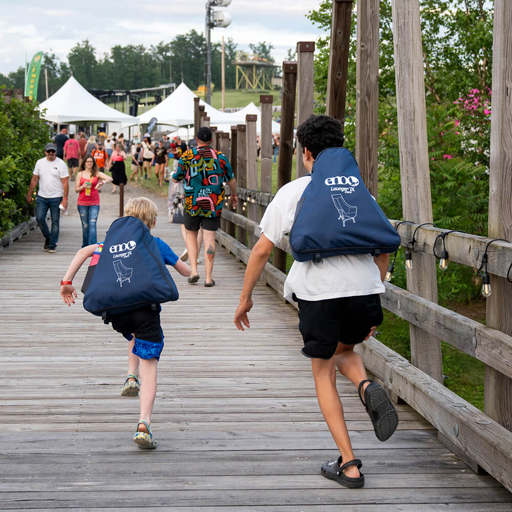 Two children run towards a festival with packed Lounger DL Chairs on their backs.